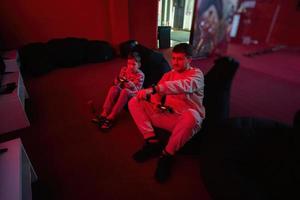 Father and son play gamepad video game console in red gaming room. Dad and kid gamers. photo