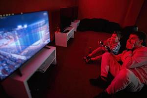 Father and son play gamepad video game console in red gaming room. Dad and kid gamers. photo
