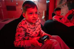 Two boys gamers play gamepad video game console in red gaming room. photo