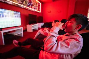 Two boys gamers play football gamepad video game console in red gaming room. Drink soda can. photo