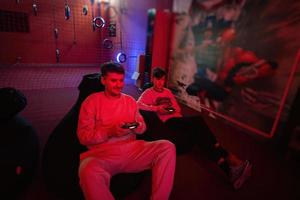 Father and son play gamepad video game console in red gaming room. Dad and kid gamers. photo