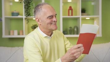 velho culto homem lendo às lar, feliz e aprendizado. a velho homem é lendo uma livro às casa feliz e Felizmente. Educação ensino conceito. video