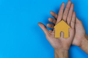 comprar o alquilar. un pequeño casa modelo hecho por papel cortar en un hombre mano en azul antecedentes. foto