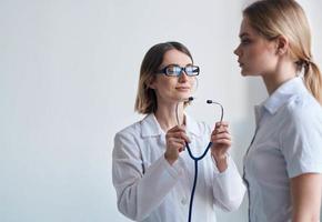 mujer médico en un médico vestido y lentes con un estetoscopio alrededor su cuello y un hembra paciente foto