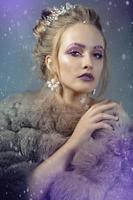 Winter girl in a fur coat in purple background. Luxurious model with beautiful makeup. Young fashionable woman. photo