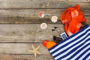 Summer clothing and accessories handbag, headphones, mobile phone, sunglasses, sunscreen on old wooden background. photo