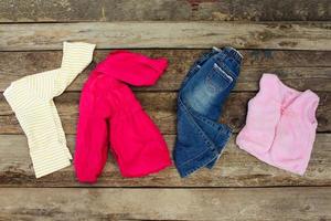 Children's clothing and accessories jeans, jacket, hair clips and warm vest on old wooden background. Top view. photo