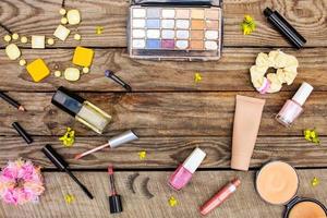 Cosmetics mascara, beads, elastic hair band, false eyelashes, concealer, nail polish, perfume, eyeliner, powder, lip gloss, eye shadow and yellow flowers on wooden background. Toned image. photo