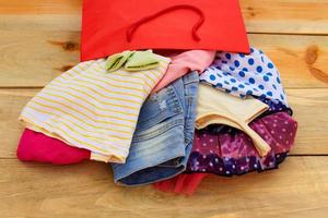 Women's clothing falls out of paper shopping bags on wooden background. photo