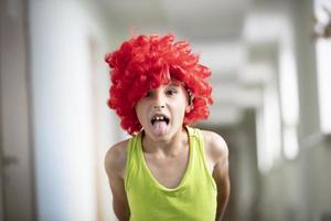 A child in a bright wig. Funny boy with red artificial hair. Bad man shows tongue. photo