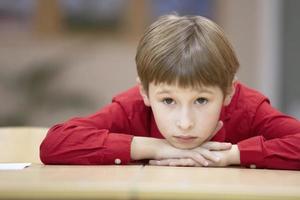 Child primary school student. A boy in a red shirt at the table. photo