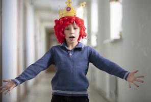 Child in a red wig and a crown. Clown boy photo