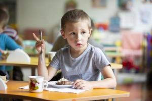 un niño come en jardín de infancia. un pequeño chico con un pobre apetito.desayuno para niños. niñito con un plato y tenedor. foto