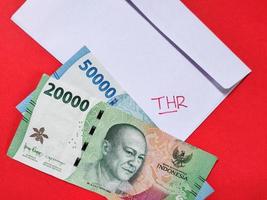 Top view of a white envelope written of THR and new Indonesian banknotes, usually Tunjangan Hari Raya or called THR are given to employees ahead of Eid. Isolated on a red background photo