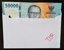 Top view of a white envelope written of THR and new Rp.50,000 Indonesian banknotes, usually Tunjangan Hari Raya or called THR are given to employees ahead of Eid. photo