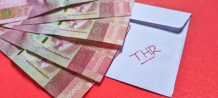 Close up view of a white envelope that written THR with Indonesian banknotes Rp.100,000 isolated on red background photo