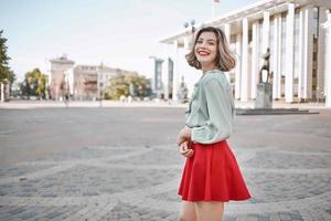 cheerful woman in a red skirt on the square in the city walk photo