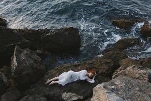 Barefoot woman in a white dress lying on a stone in a white dress view from above photo