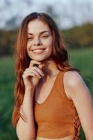 Close-up portrait of a smiling young woman in the sun with red hair in nature photo