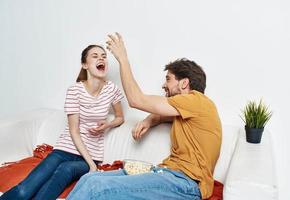 cheerful man and woman on the couch with popcorn and red plaid flower in a pot emotions photo