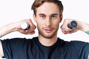 a sporty man in a black t-shirt holds dumbbells near his face on a light background and a black t-shirt photo