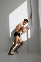 sexy man with a cup of muscular body in black panties is holding on to the wall photo