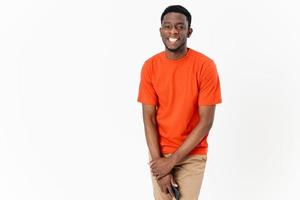 African guy in an orange T-shirt with a mobile phone and in trousers on a light background photo