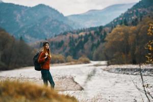 joven viajero con un mochila en pantalones y un suéter cerca el río en el montañas foto