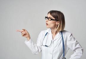 woman nurse in a medical gown gesturing with her hands on a light background copy space photo