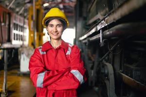 Ingenieria mujer en la seguridad uniforme operando máquina a fábrica industrial y en pie con sonriente en lugar de trabajo foto