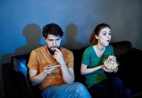 un mujer y un hombre con palomitas de maiz en un cuero sofá adentro acecho televisión en el noche foto