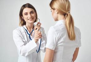 doctor with a stethoscope examines a woman in a white t-shirt on a light background photo