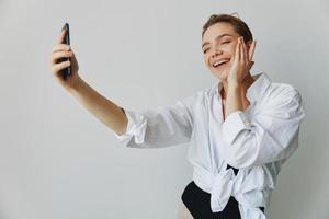 Teenage girl blogger takes photos and shoots. herself on video on her phone for social media content, video blogger, selfies against a white wall with a smile at home, freelancer
