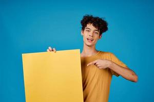 guy with curly hair holding a yellow poster in his hands advertising photo