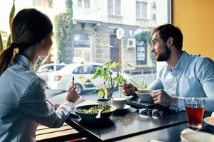 negocio hombre y mujer en un camisa teniendo almuerzo a un mesa en un café restaurante cerca el ventana foto