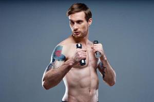 guy with a pumped up torso and with dumbbells on a gray background cropped view of the press and biceps fitness photo