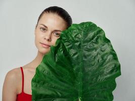 young woman in red t-shirt on light background with green leaf of palm tree cropped view photo