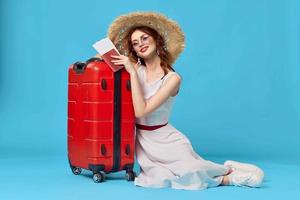 bonito mujer en sombrero sentado en el piso con rojo maleta viaje destino foto