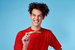 energético chico con un rebanada de Pizza teniendo divertido en un azul antecedentes y un rojo camiseta foto