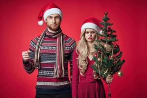 man and woman standing next to christmas tree toys lifestyle red background photo