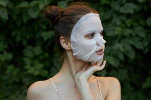 bonito niña cosmético máscara sostiene su mano cerca su cara y mira lejos desnudo espalda hojas en el antecedentes foto