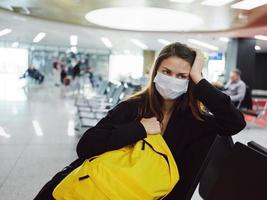 mujer con amarillo mochila en médico máscara esperando para vuelo foto