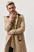 pensive blond man in beige coat holds hand near face portrait photo