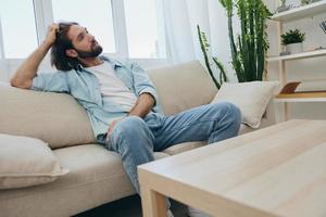 A young male freelancer sits on the couch after a demanding job and rests sadly leaning on the couch. photo