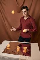 a man in a red shirt with oranges near the table with a mirror photo