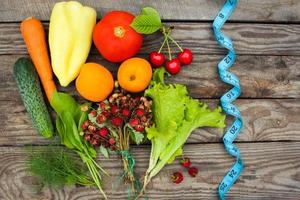 Fruits, vegetables and in measure tape in diet on wooden background photo