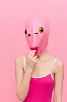 Funny woman in a sexy costume with a pink fish mask on her head put her fingers in her mouth in pink clothes on a pink background. The concept of modern art photography photo