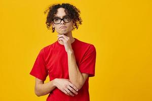 Pensive thoughtful myopic young student man in red t-shirt funny eyewear posing isolated on over yellow studio background. The best offer with free place for advertising. Education College concept photo