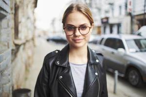 Fashionable woman in a leather jacket and glasses on the street and cars on the road photo