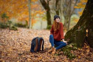 a woman in warm clothes in the fall sits near a tree in the forest photo